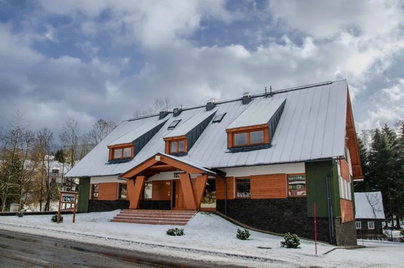 Pension Troll mit Holzeingang und Schnee vor dem Haus